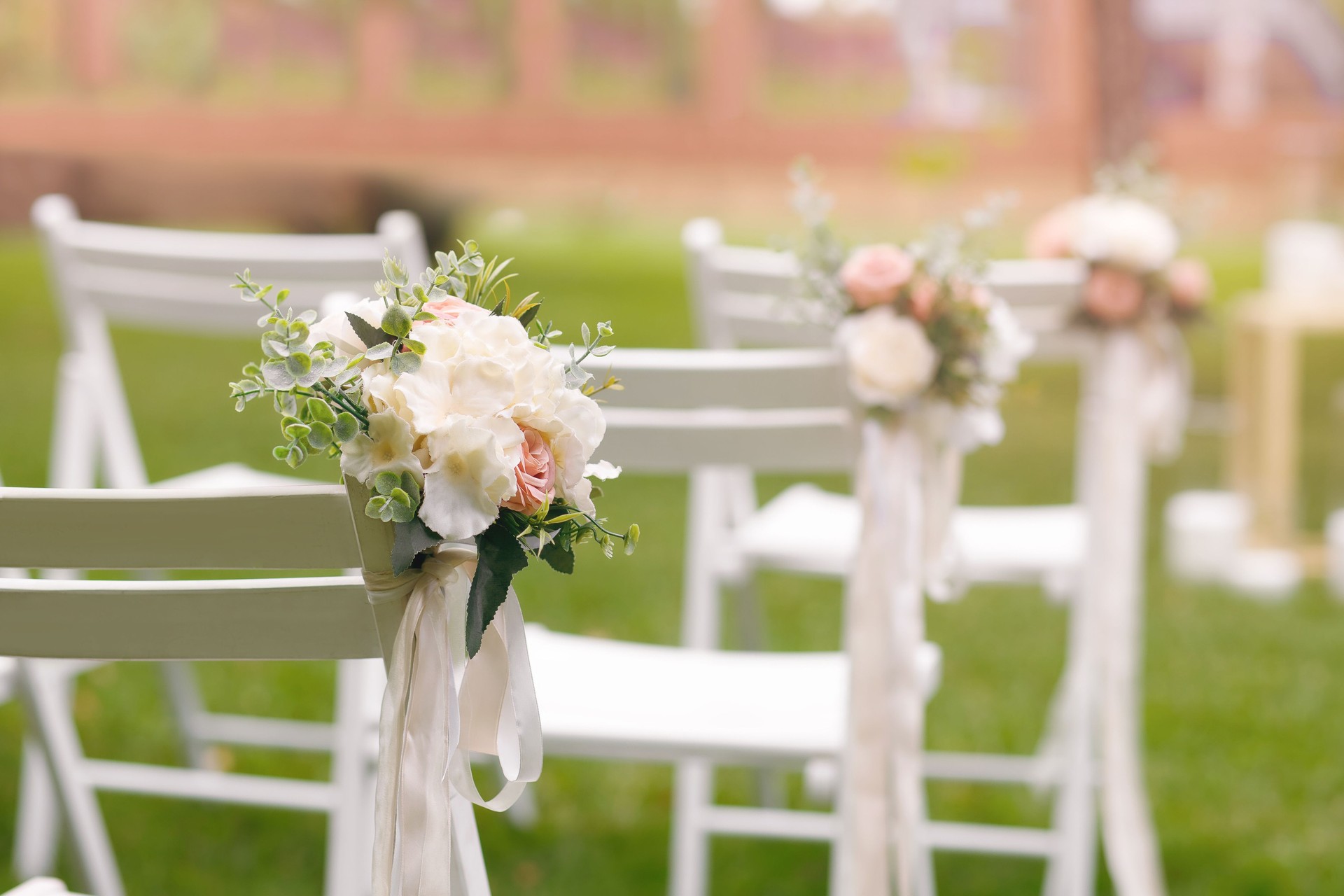 White chairs decorated with flowers on a green lawn for a wedding ceremony